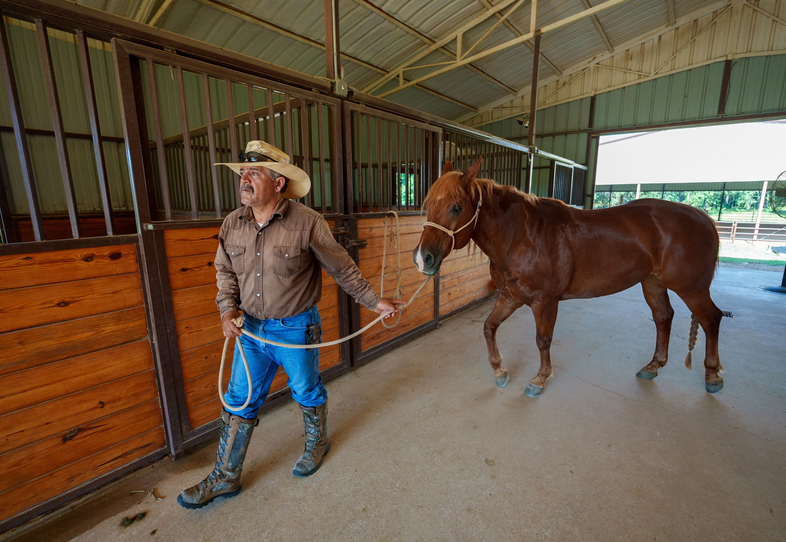 man leading a horse through a barn